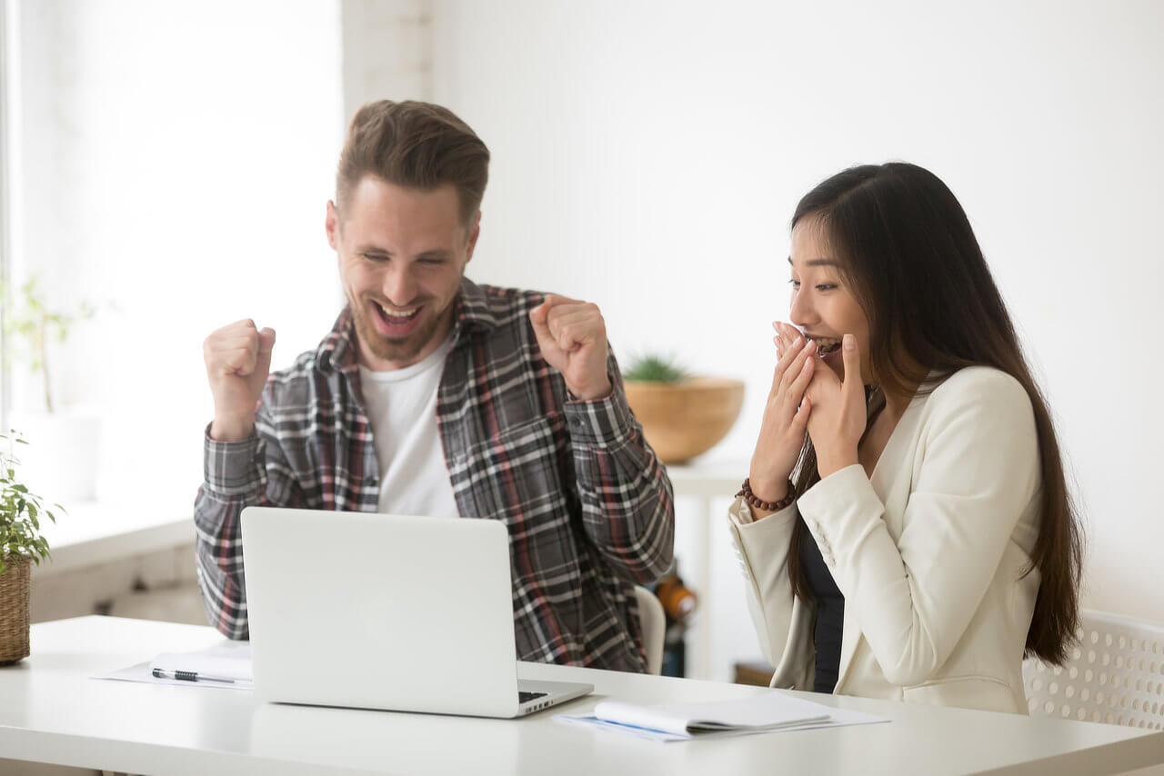 man and woman looking at laptop expressing success and excitement
